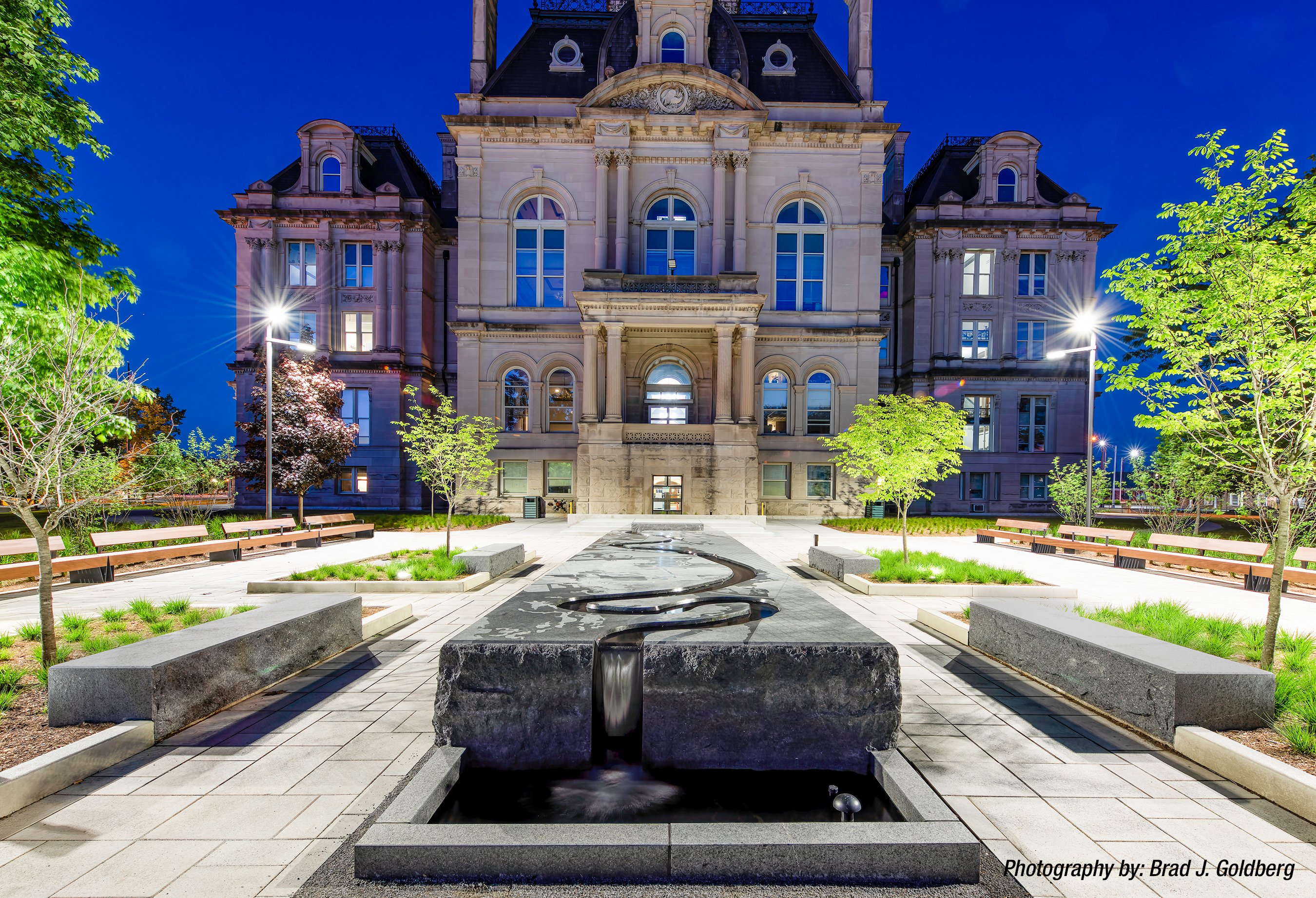 A nighttime view of city hall in front on the black granite fountain sculpture