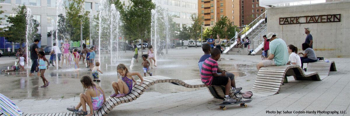 Group of children and family surrounding a large fountain project at Park Tavern